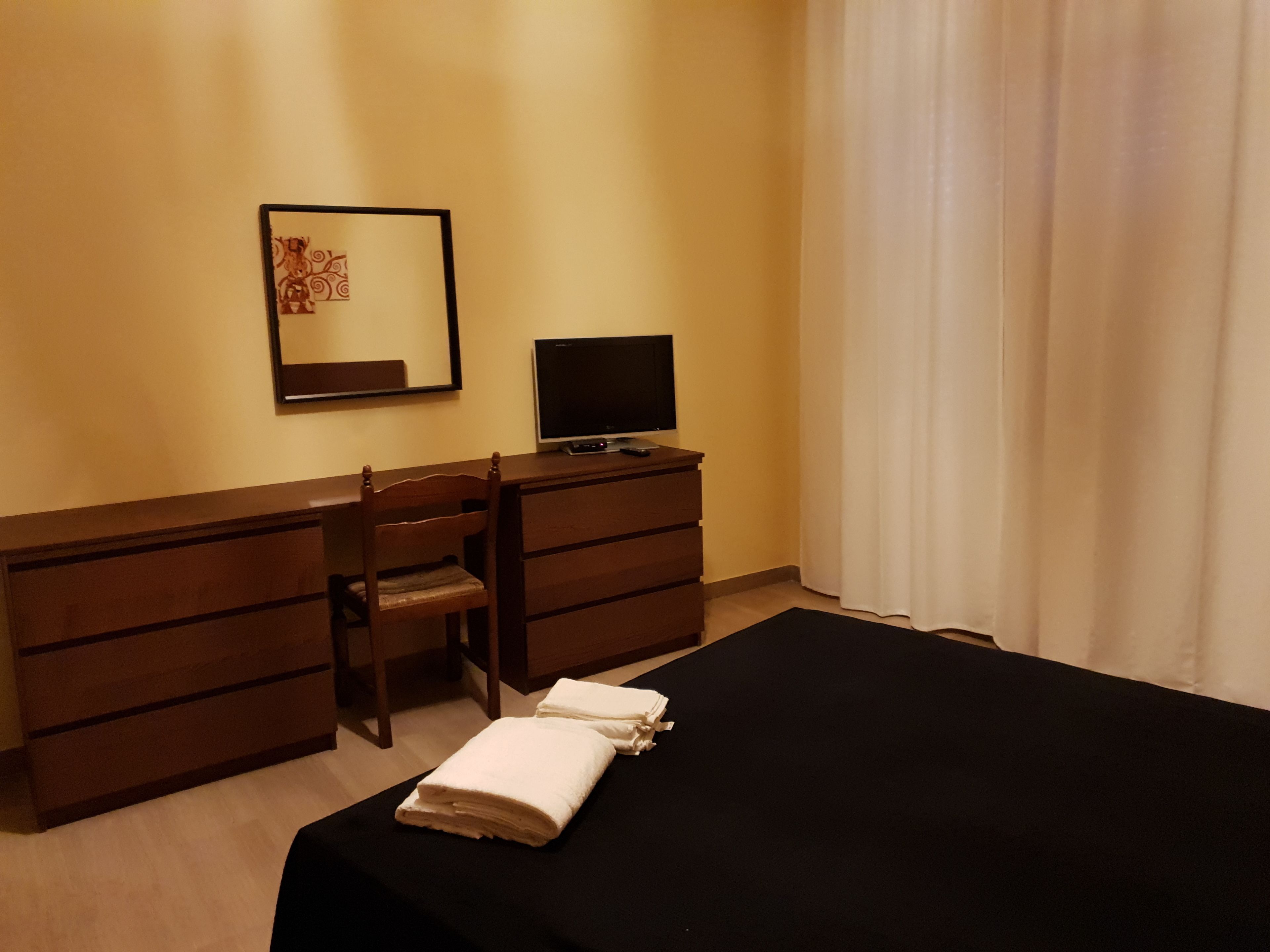 A hotel room with a bed, a desk with a chair, a television, and a framed picture on the wall.