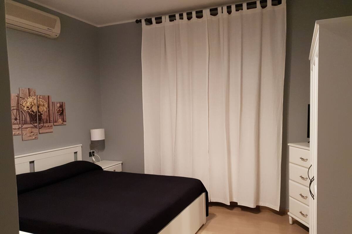 A bedroom with a bed, a nightstand, a lamp, a wardrobe, and a curtain.