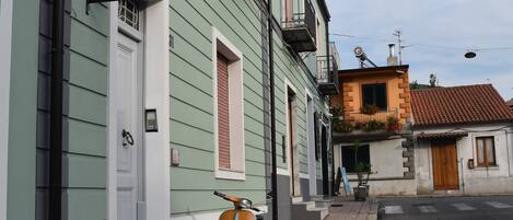 A narrow street with a vintage scooter parked by a building with a sign reading "B&B El Paso del Mercante".