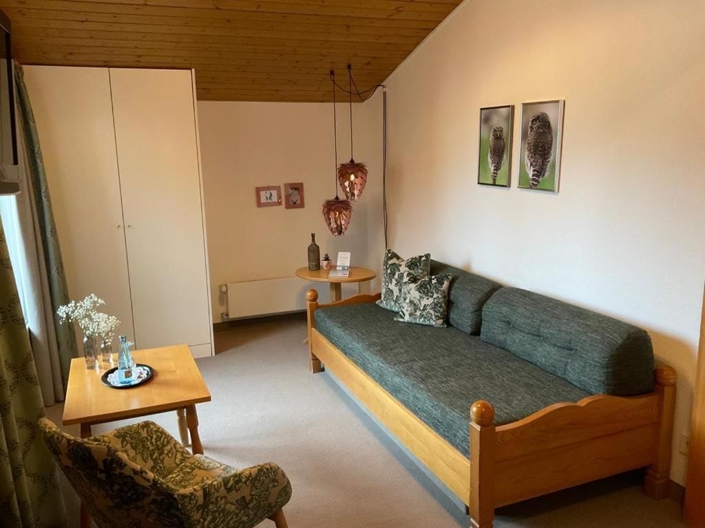 A room with a wooden bed, a small table with a vase, a chair, and two framed pictures on the wall.