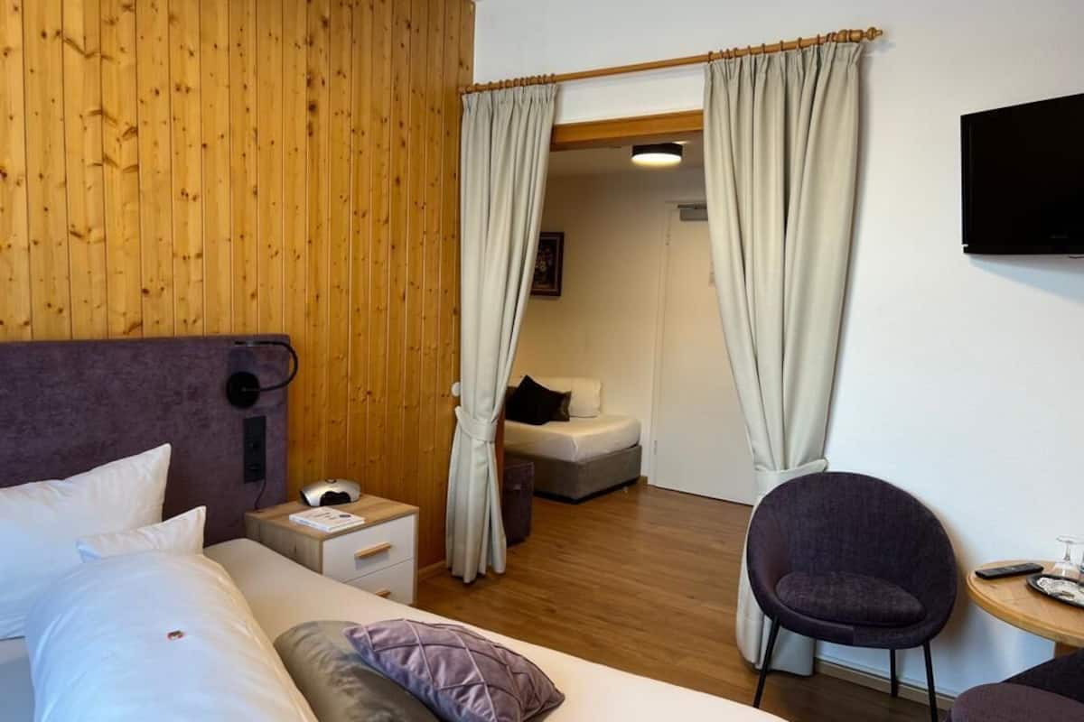 Een hotelkamer met een houten wand, een bed met wit beddengoed, een bureau met een stoel en een televisie aan de muur.