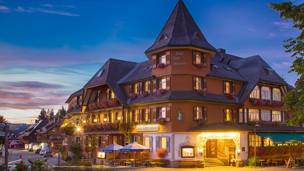 Een groot, meerlaags hotel met een opvallende toren, meerdere balkons met bloembakken en buiten zitgedeeltes.