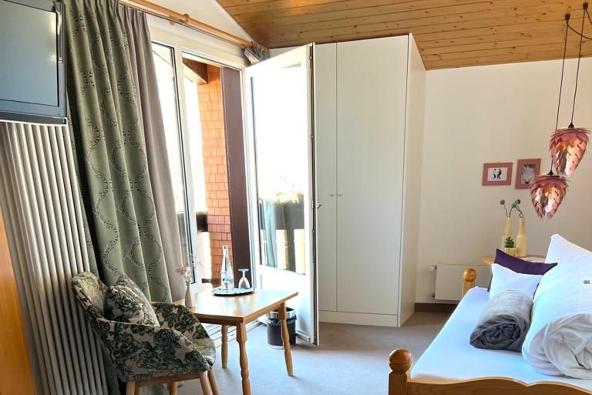 A bedroom with a bed, a chair, a table, and a TV.