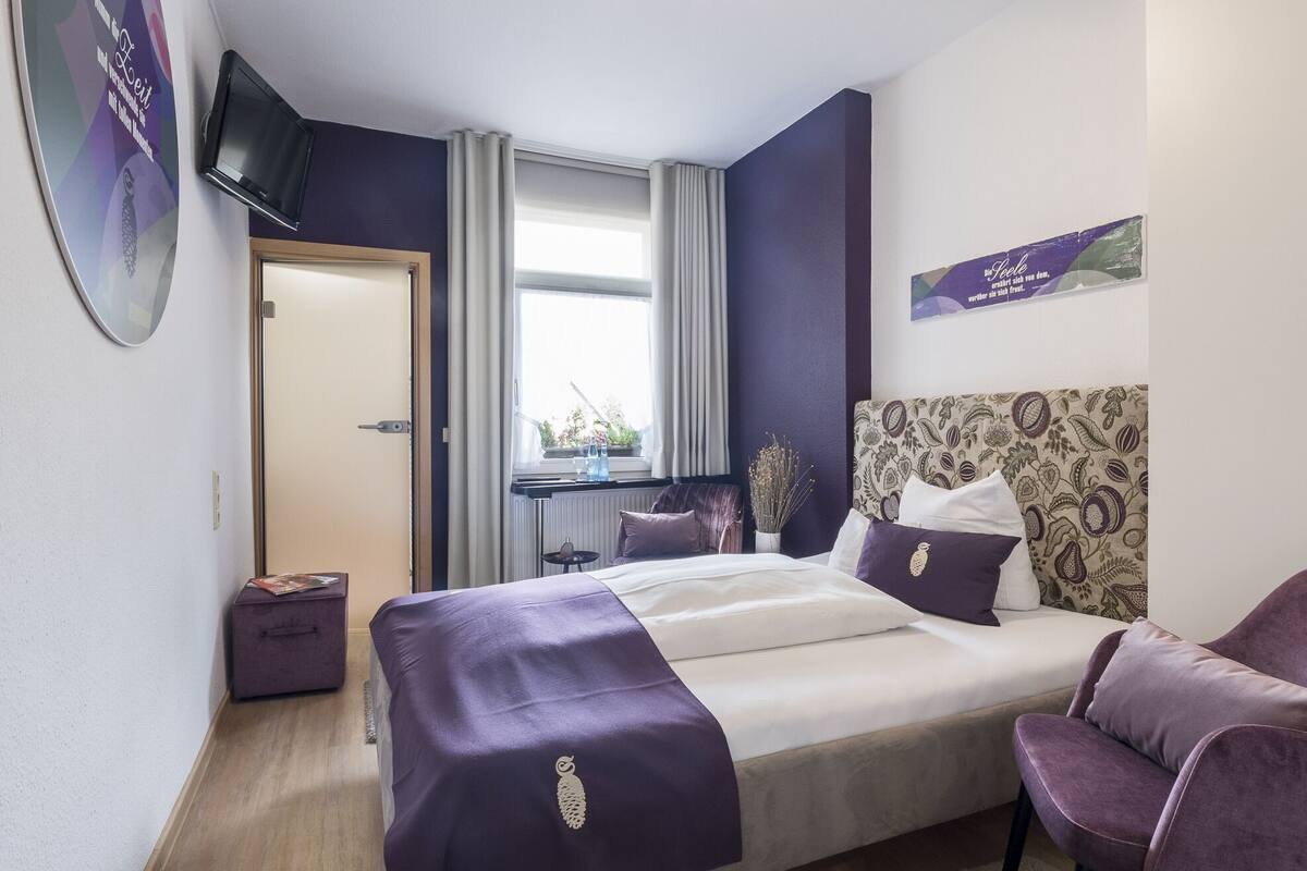 Een slaapkamer met een bed, een stoel, een televisie, een raam en een deur.