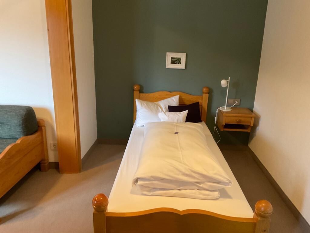 Ein Einzelbett mit Holz Kopfteil, ein Nachttisch mit Lampe und ein gerahmtes Bild an der Wand.