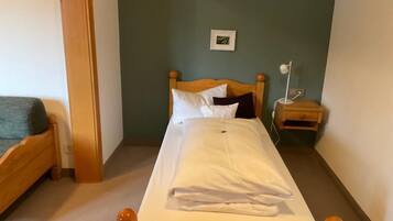 Ein Einzelbett mit Holz Kopfteil, ein Nachttisch mit Lampe und ein gerahmtes Bild an der Wand.