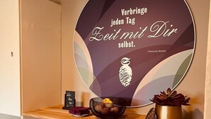 Een kamer met een ronde spiegel, een klein plantje en een plank met diverse spullen, waaronder een kom, een fles en enkele tijdschriften.