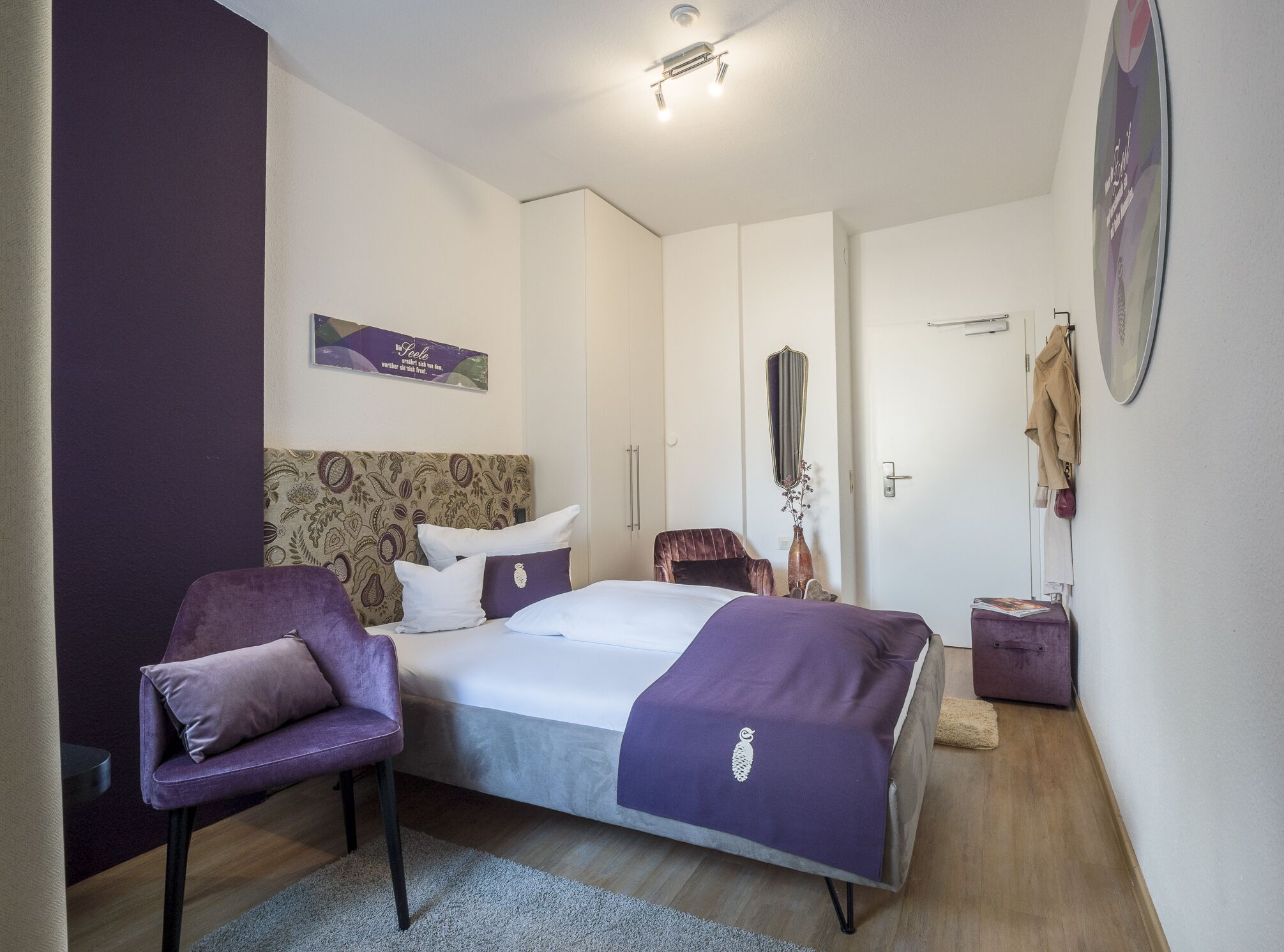 Un dormitorio con cama, una silla, una mesita de noche y un espejo.