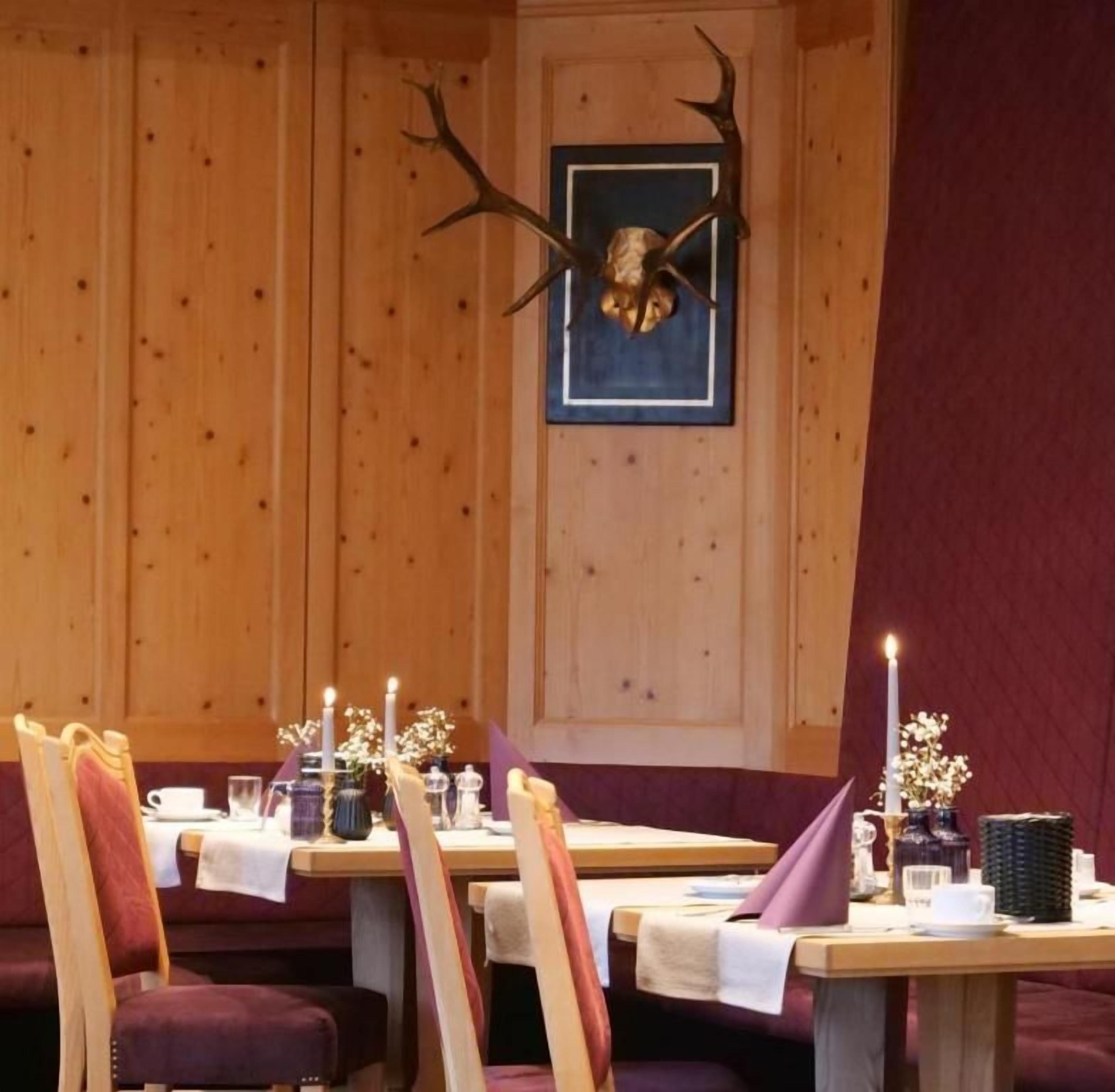 Ein Essbereich mit Holzwandverkleidung, einem aufgehängten Hirschgeweih und einem Tisch, der mit Kerzen und Blumen gedeckt ist.