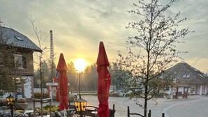 Een terras met tafels en stoelen, omringd door plantenpotten en rode parasols.