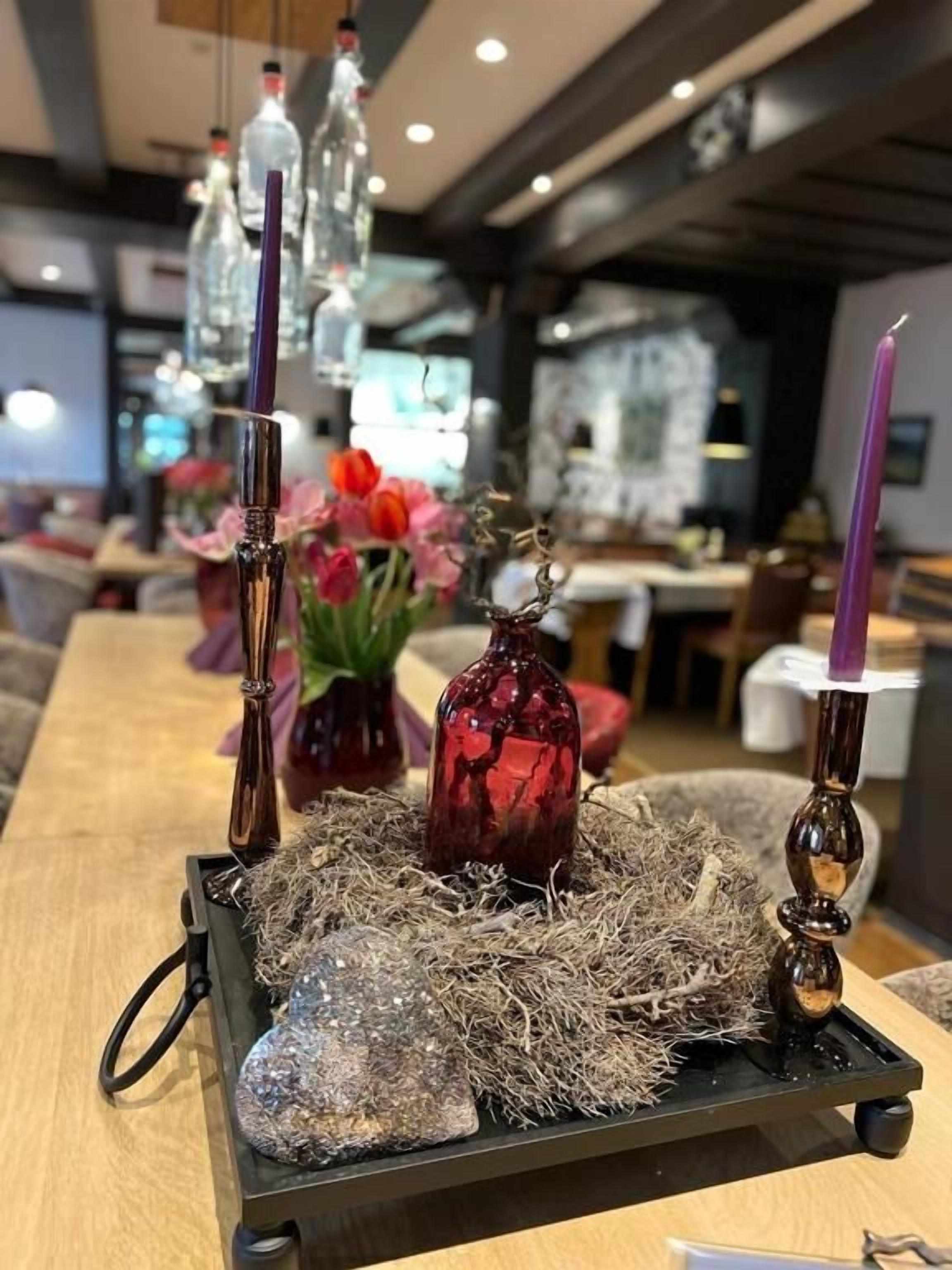 Un tavolo con un centrotavola decorativo con candele, una bottiglia di vetro e un vaso con fiori.