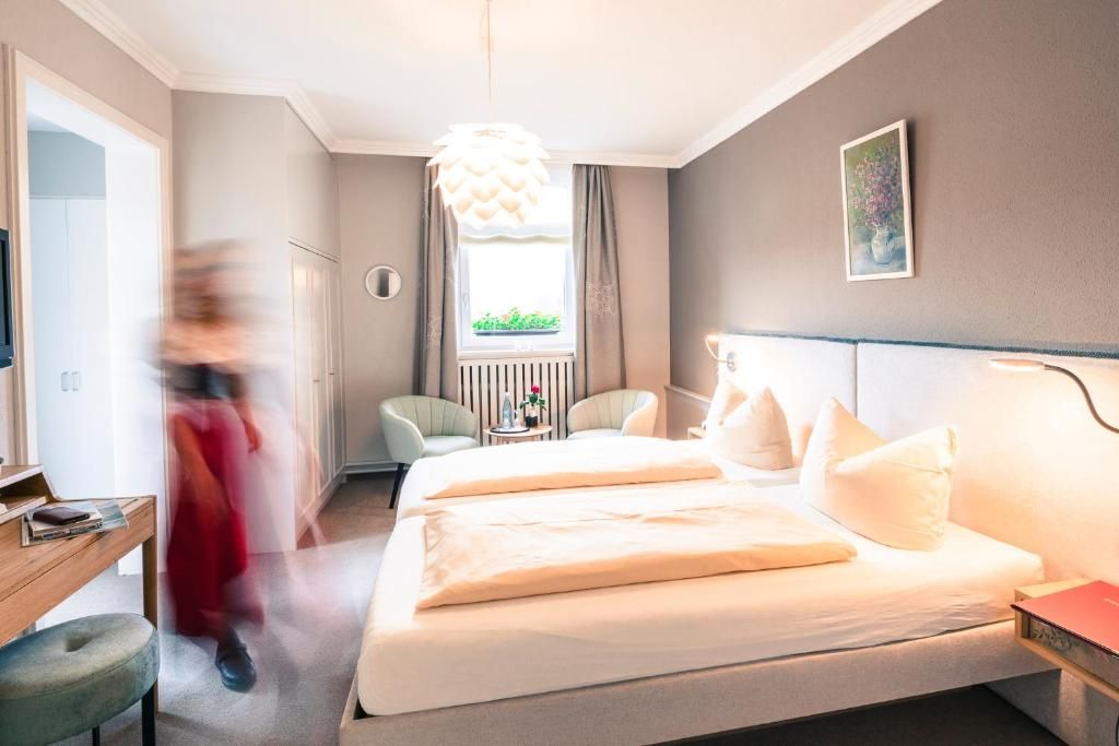 Ett hotellrum med en säng, ett sängbord, en stol och ett fönster med gardiner.