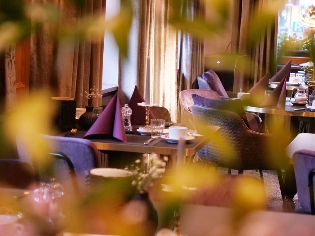 Un restaurant où les tables sont dressées pour le service, avec des chaises violettes et brunes, et une ambiance chaleureuse et accueillante.