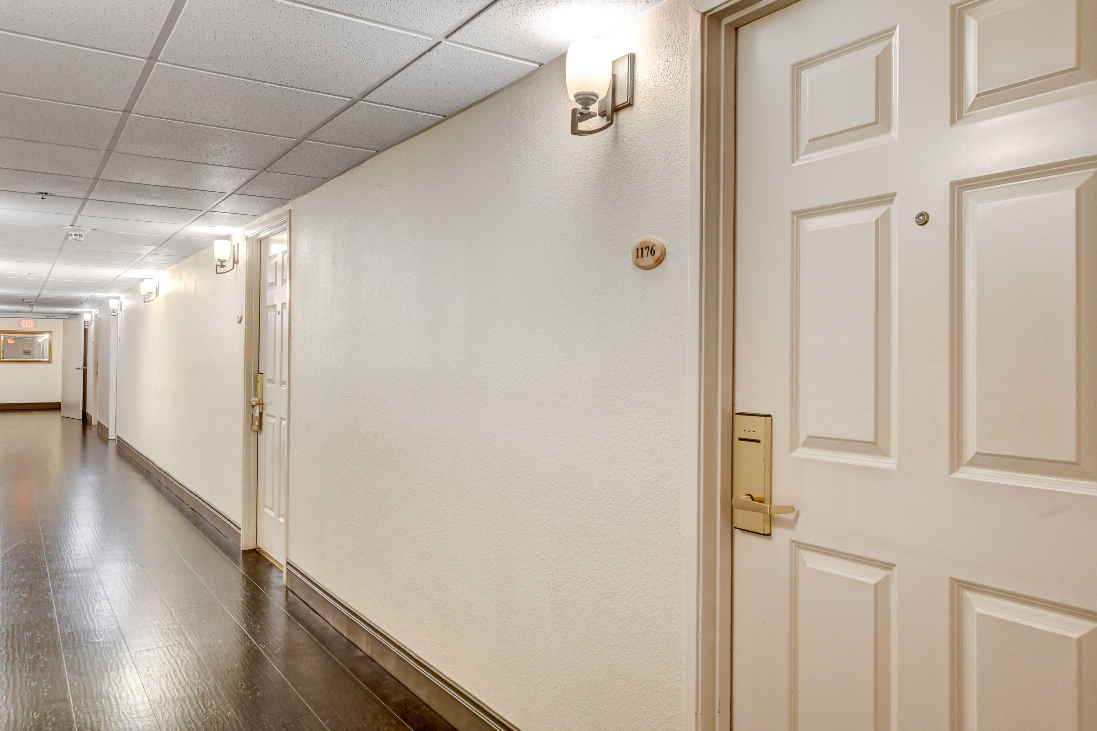 A hotel hallway with white walls, a wooden floor, and doors with a number plate.