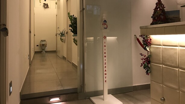 Un corridoio d'albergo con una reception, un cartello che recita 'IGIENZANTE' e una ghirlanda decorativa al muro.