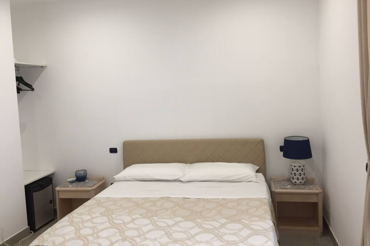 A hotel room with a bed, two bedside tables, a lamp, and a small cabinet.