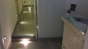 Un corridoio stretto con una porta in vetro che dà su una stanza. Si intravede a destra un piccolo bancone con una vetrina.