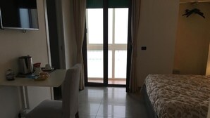Una camera d'albergo con un letto, una scrivania, una sedia, un televisore e vista all'esterno tramite una porta scorrevole.