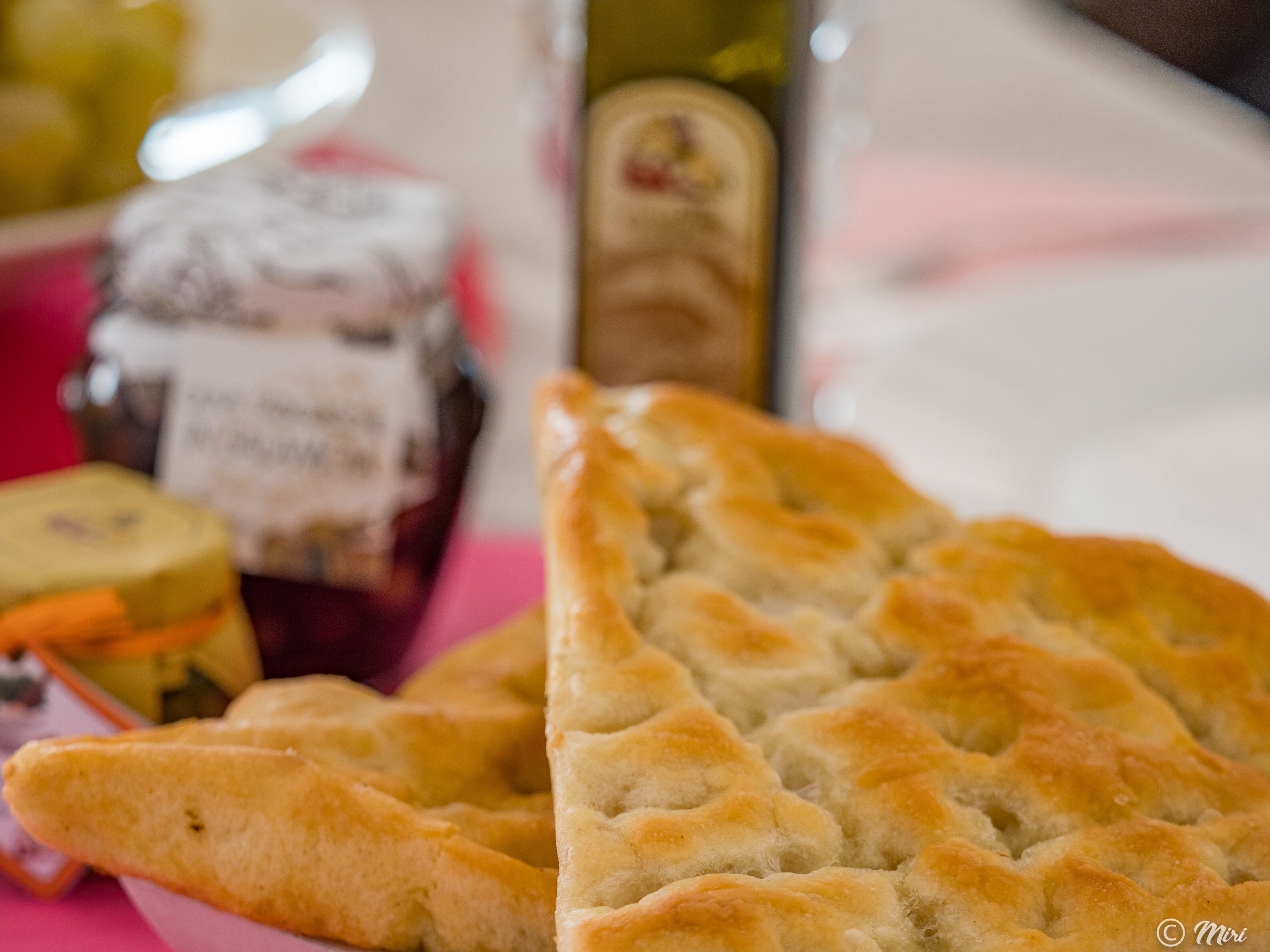 A close-up of a baked good with a golden-brown crust, possibly a type of bread or pastry, on a table with a pink surface.