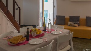 A dining area with a table set for two, a bottle of wine, and a bowl of fruit. There is a staircase to the left and a sofa with cushions in the background. - El Nin Apartment with Terrace & AC (Vernazza)