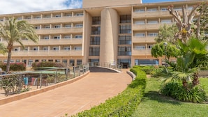 A large, multi-story hotel with a central courtyard, palm trees, and a clear blue sky. - Aparthotel Club Cala Romaní (Cales de Mallorca)