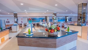 A modern hotel lobby with a central reception desk, seating area, and a view of the sea through the windows. - Aparthotel Club Cala Romaní (Cales de Mallorca)