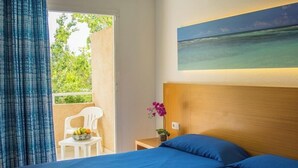 Habitación de hotel con una cama, una mesita con fruta, una silla y vistas al exterior.