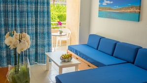 A room with a blue sofa, a white table with a fruit bowl, and a painting of a beach scene. - Aparthotel Club Cala Romaní (Cales de Mallorca)