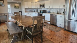 A modern kitchen with white cabinets, stainless steel appliances, and a wooden dining table with chairs. - Wine Country Farmhouse Private Lake! kayaks Fire Pit! On The Wine Trail! (Cobden)