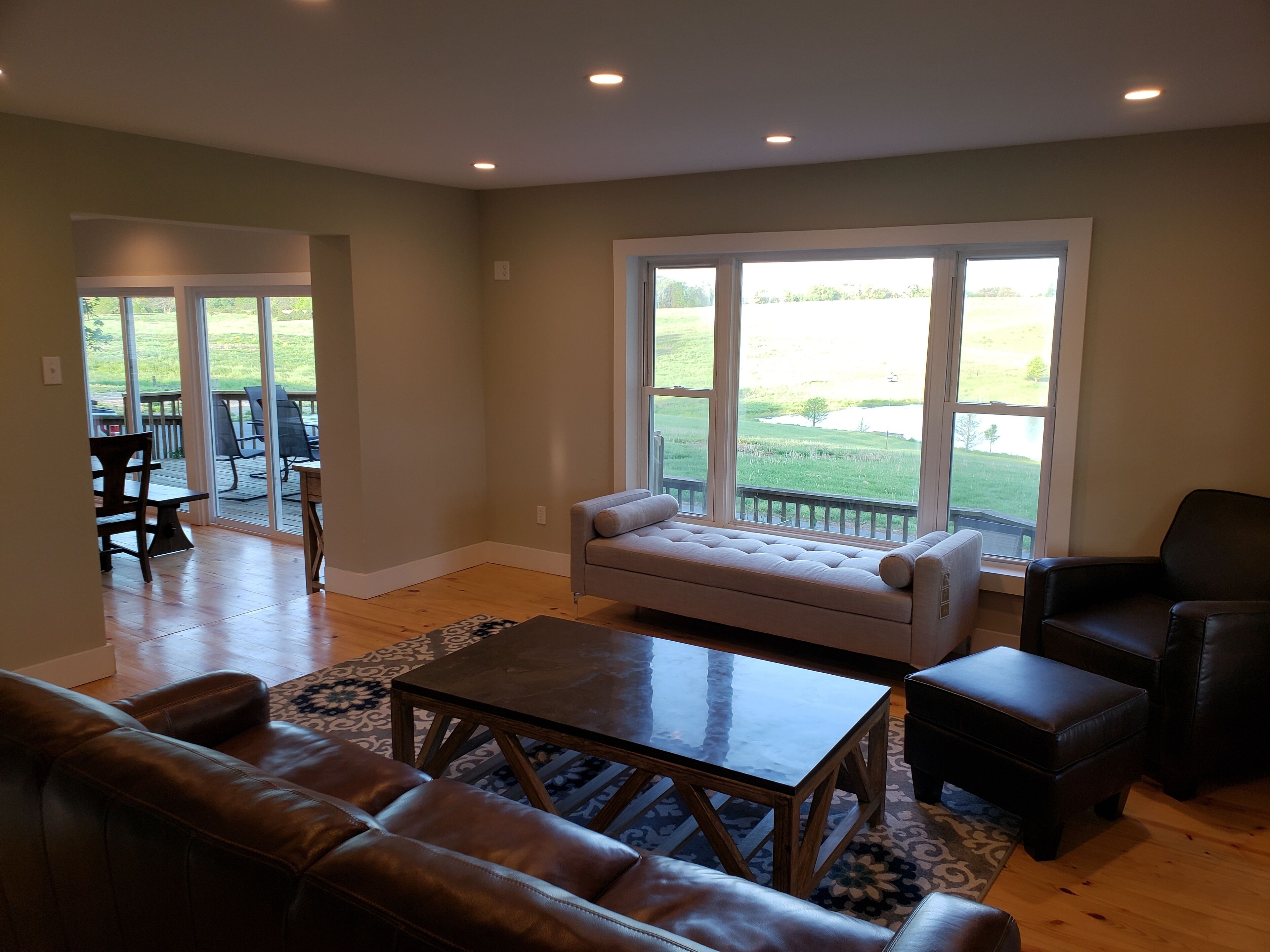 A spacious living room with a leather sofa, a glass coffee table, and a view of a grassy outdoor area through large windows.