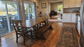 A spacious kitchen with wooden flooring, a dining area with a large table and chairs, and a view of the outdoors through large windows. - Wine Country Farmhouse Private Lake! kayaks Fire Pit! On The Wine Trail! (Cobden)