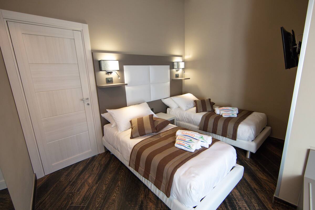 Habitación de hotel con dos camas, una puerta y una mesita de noche con lámparas.