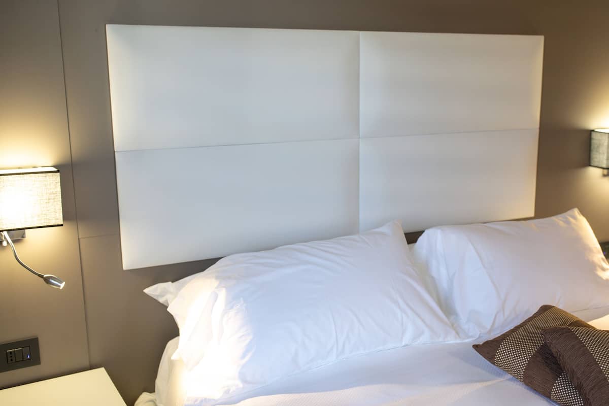 Una habitación de hotel con una cama grande, ropa de cama blanca, un cabecero con panel de luz y dos lámparas de noche.