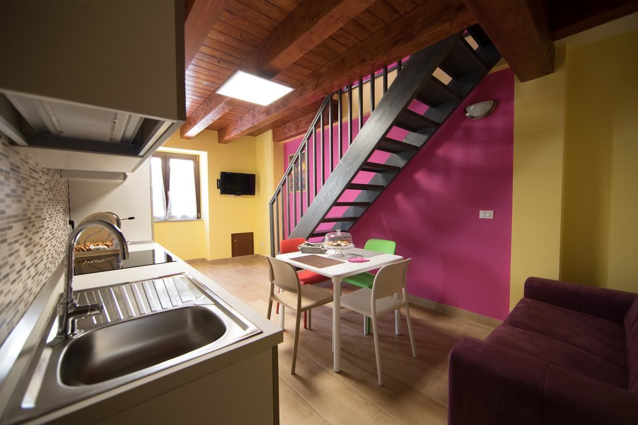 Eine kleine Küche mit Spüle und einem Essbereich inklusive Tisch und Stühlen. Eine Treppe mit pinker Geländer führt auf eine erhöhte Ebene.