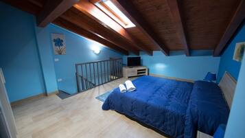 Un dormitorio con techo inclinado, una cama, un televisor y un escritorio pequeño.
