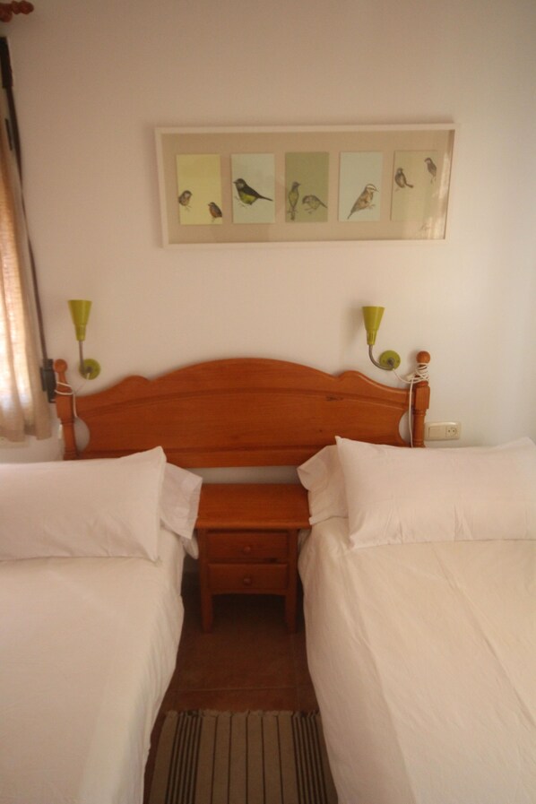 Una habitación con una cama de madera, dos mesitas de noche, un pequeño banco y un cuadro de aves colgado en la pared.