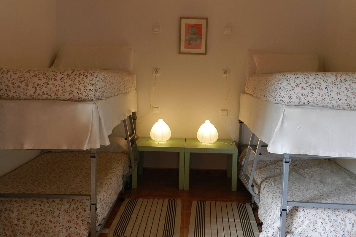 A dormitory room with bunk beds, a green nightstand with two lamps, and a framed picture on the wall.