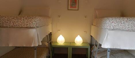 Un dormitorio con literas, una mesita de noche verde con dos lámparas, y un cuadro en la pared.