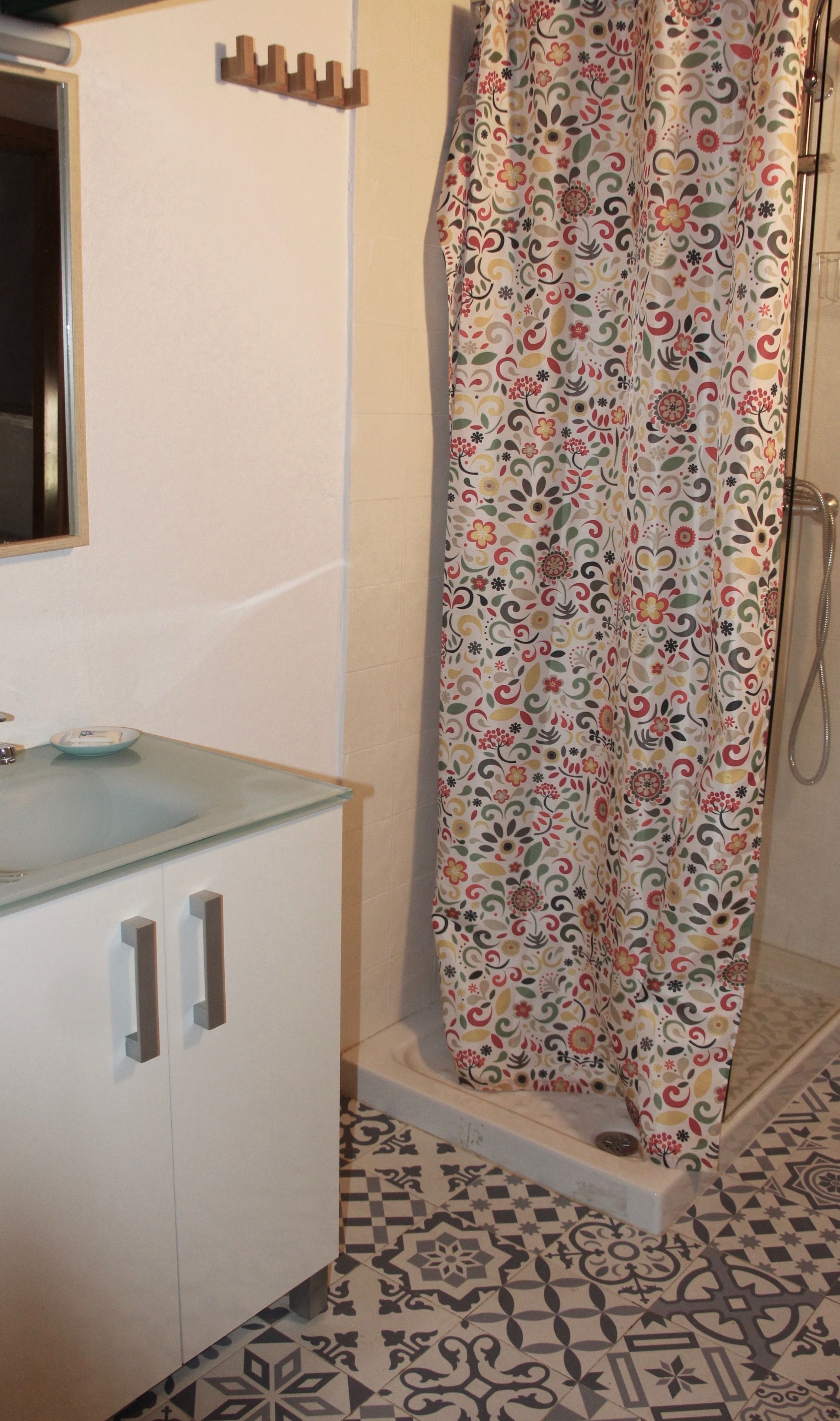 A bathroom with a shower curtain featuring a floral pattern, a glass sink, and a tiled floor with a geometric design.