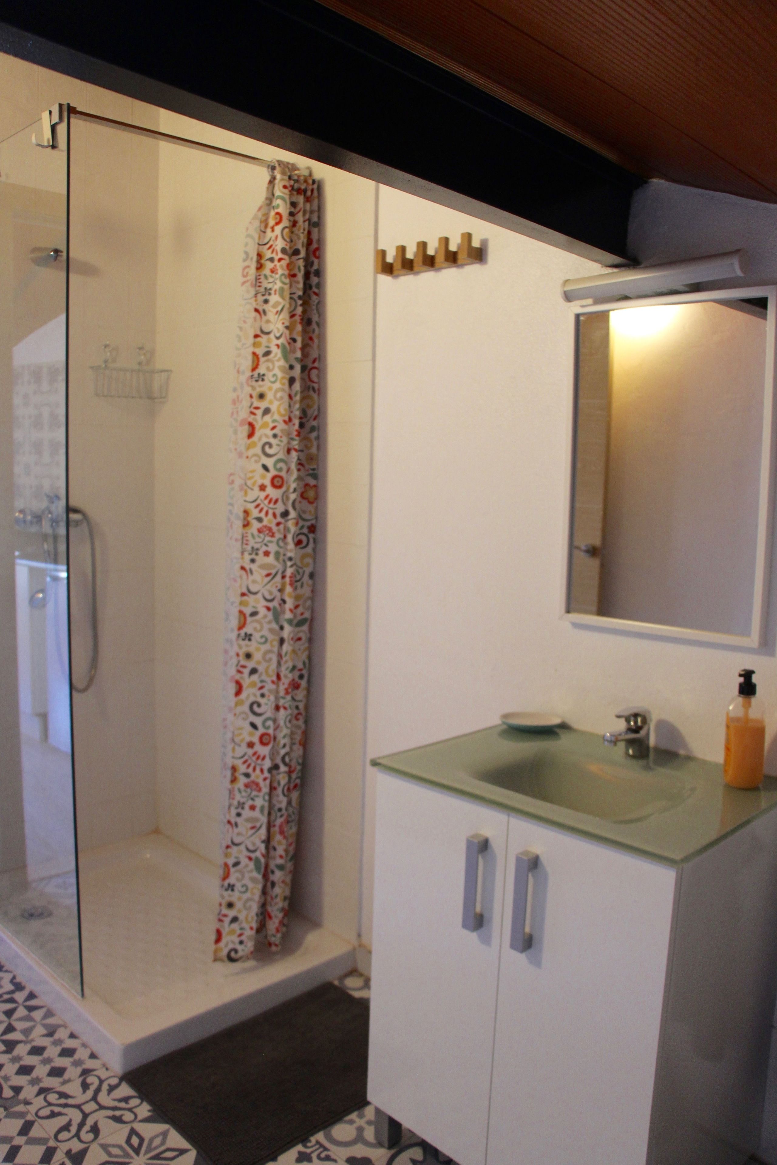 A bathroom with a glass-enclosed shower, a white cabinet with a mirror, and a sink with a soap dispenser.