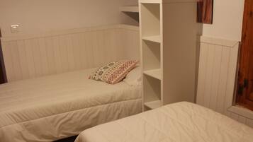 Un dormitorio con dos camas, un tapete a rayas y un estante blanco.