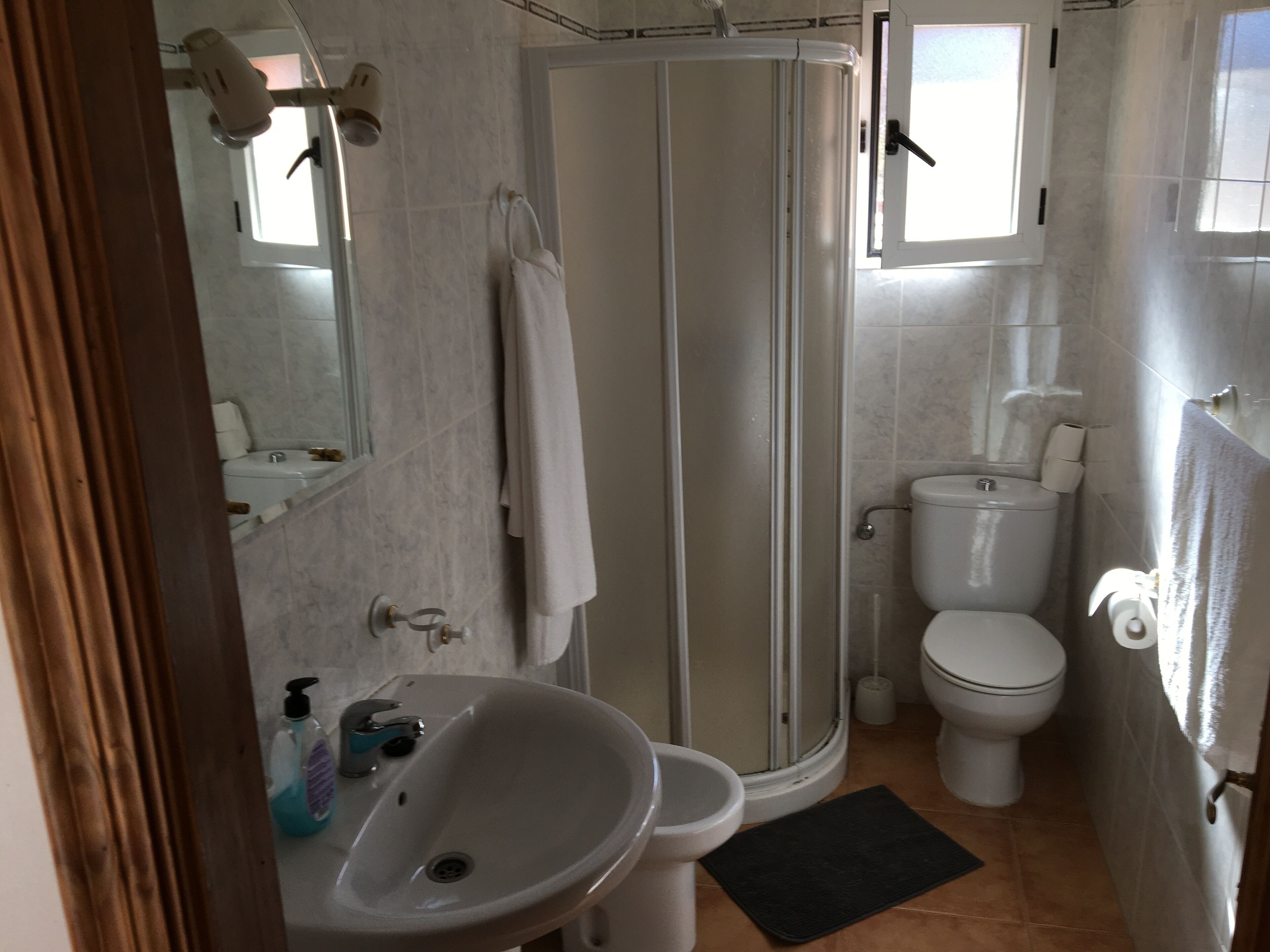 A bathroom with a shower, toilet, sink, and a mirror.