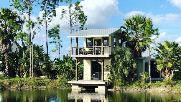 Een tweelaags huis met een balkon, omringd door water en tropische begroeiing.