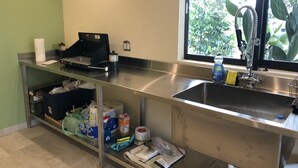 Een keuken met een roestvrijstalen spoelbak, een raam met uitzicht op groen en diverse keukenspullen op het aanrecht.