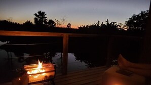 Iemand ontspant in een ligstoel met een barbecue en een kaars, met uitzicht op een wateroppervlak.