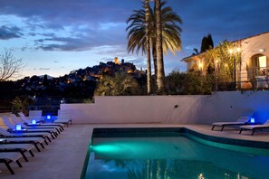 A pool area with lounge chairs and a view of a hill with buildings. - La Bastide de Biot (Biot)