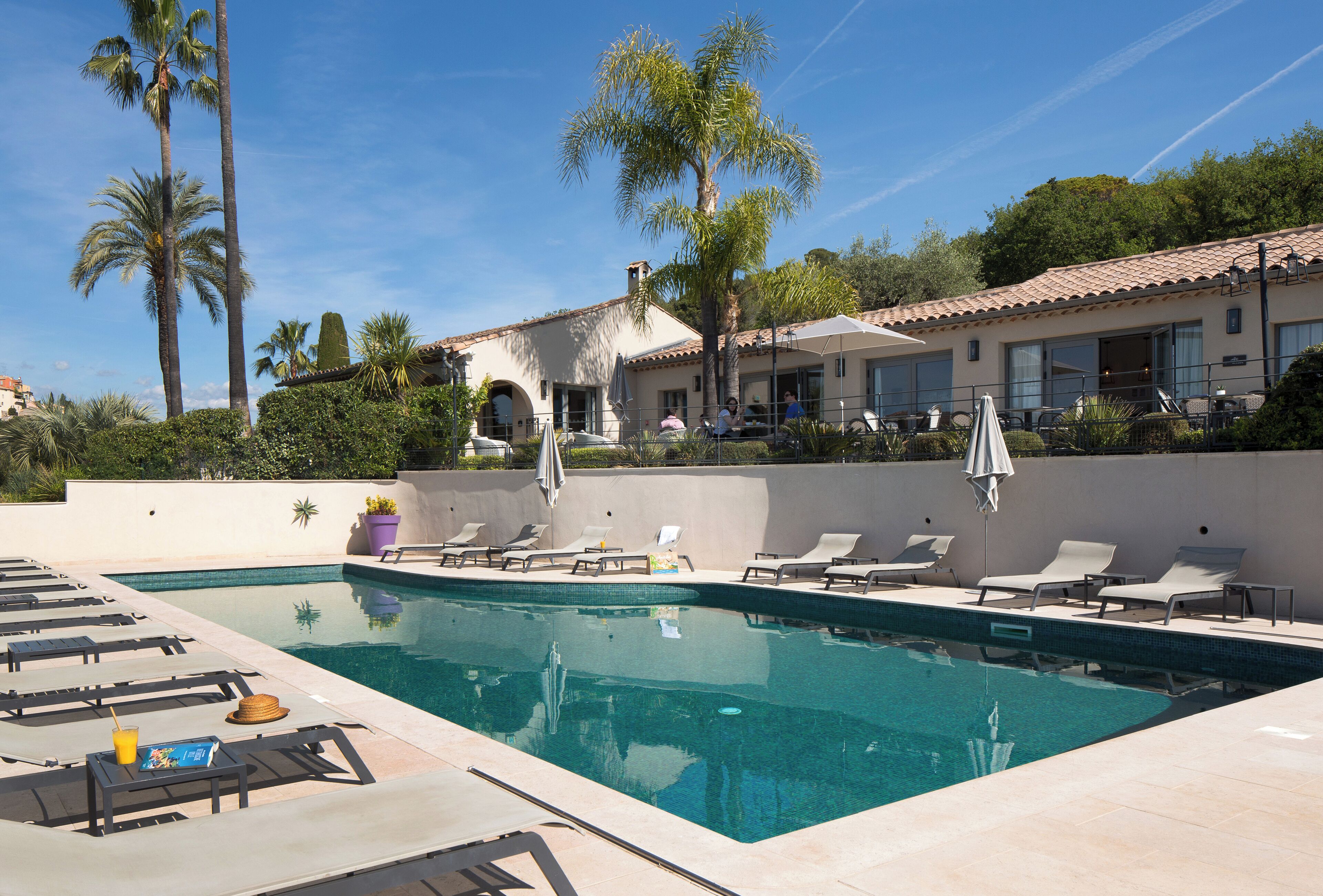 A pool area with lounge chairs, a swimming pool, and a building with a tiled roof.