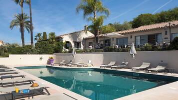 A pool area with lounge chairs, a swimming pool, and a building with a tiled roof.