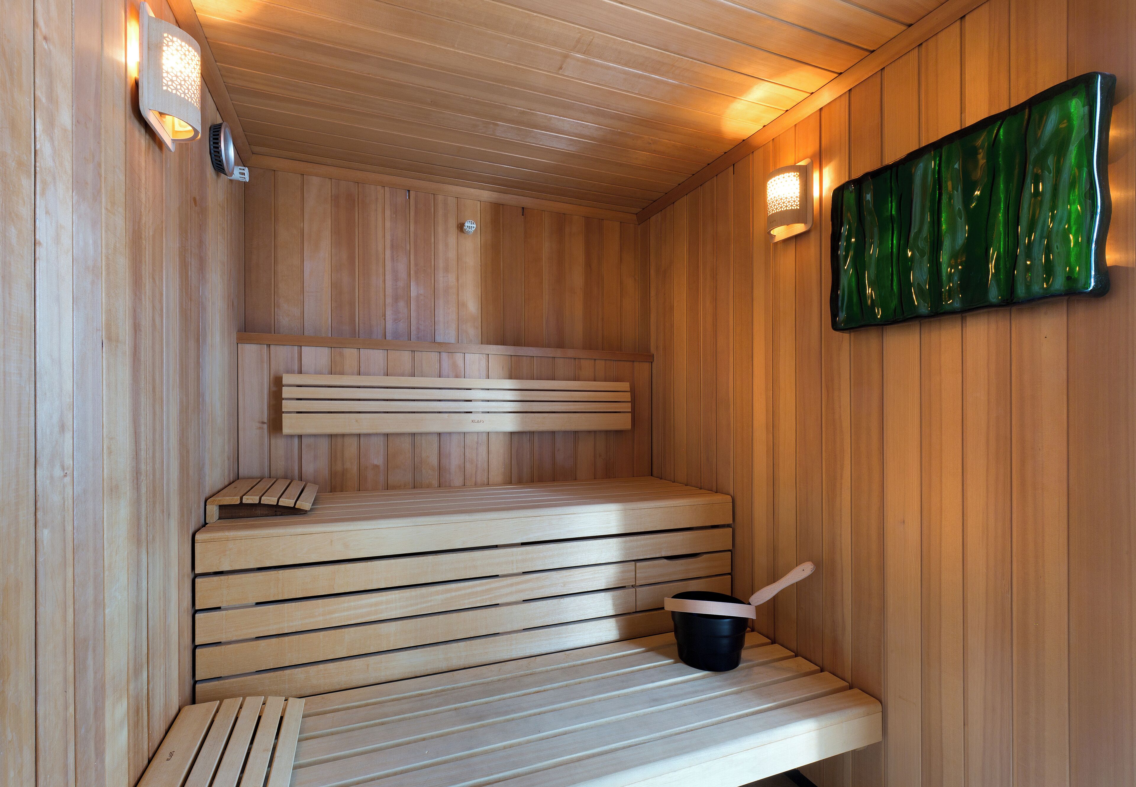 A sauna with wooden benches, a wall-mounted light, and a green decorative piece.