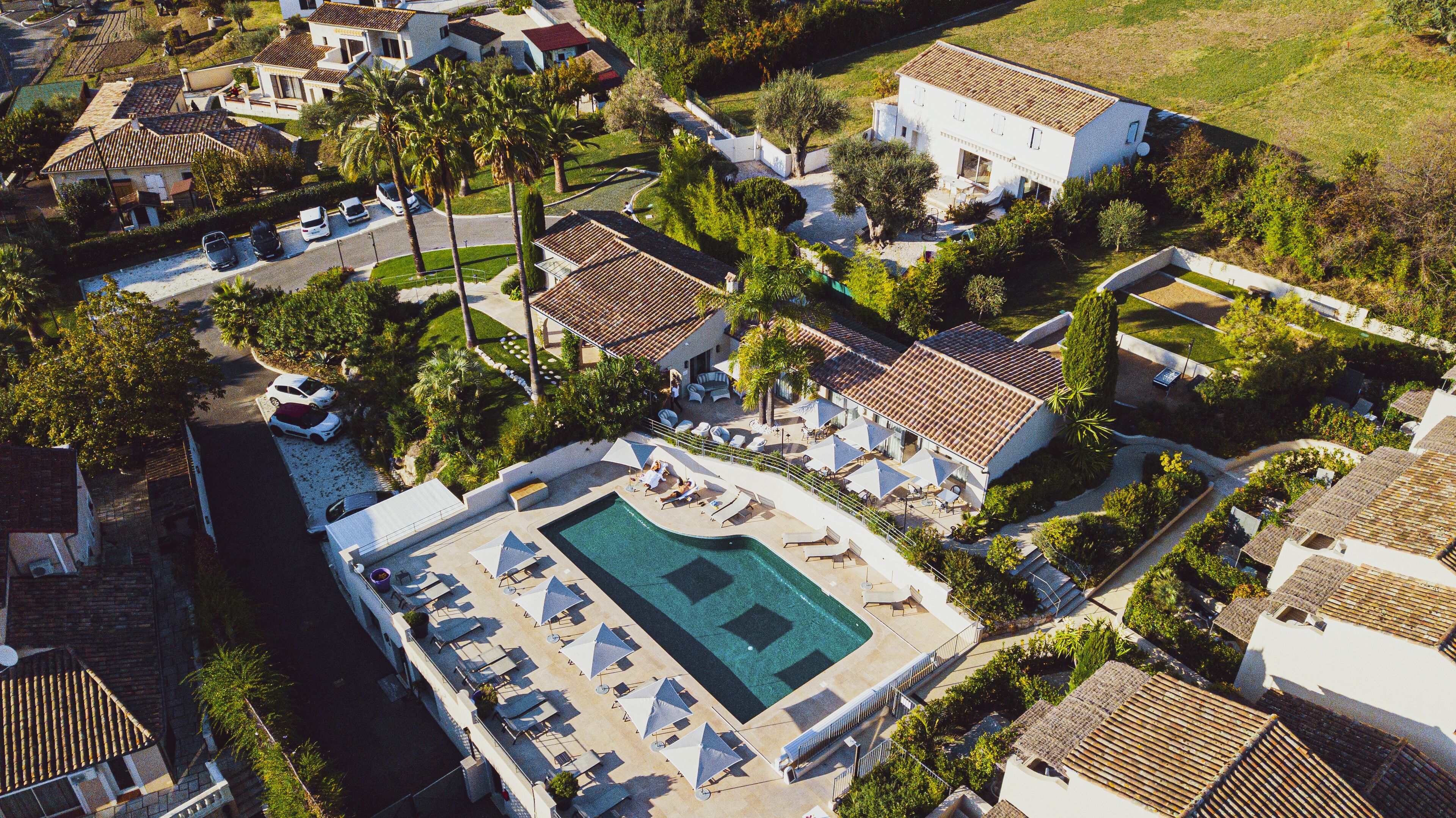 An aerial view of a resort with a swimming pool, lounge chairs, and a well-maintained garden.